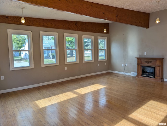 unfurnished living room featuring beam ceiling, a healthy amount of sunlight, a textured ceiling, and light hardwood / wood-style flooring