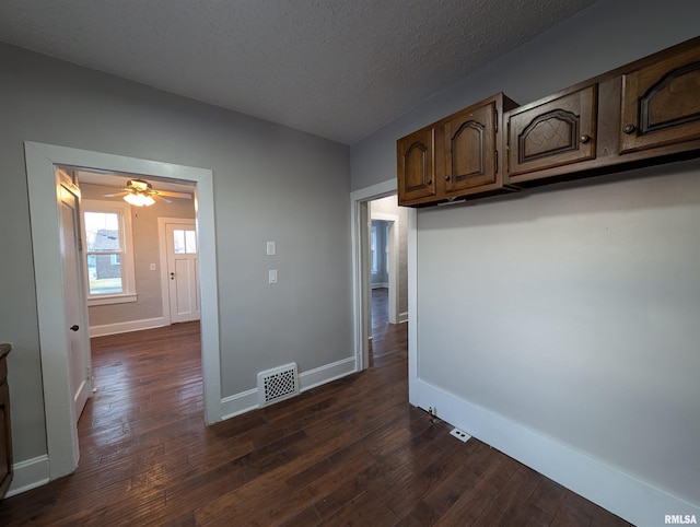 interior space with dark wood-style flooring, visible vents, a textured ceiling, and baseboards