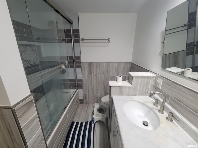 full bathroom featuring vanity, toilet, enclosed tub / shower combo, tile walls, and wood-type flooring