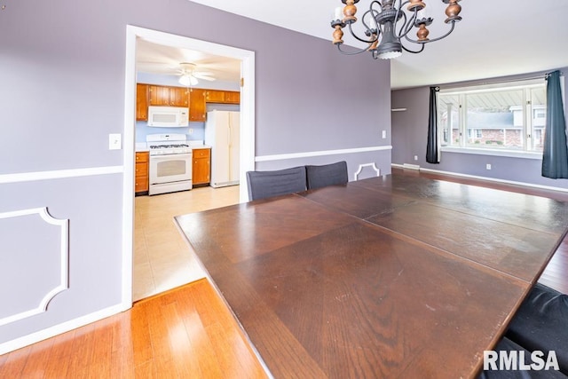 unfurnished dining area featuring ceiling fan with notable chandelier and light hardwood / wood-style flooring