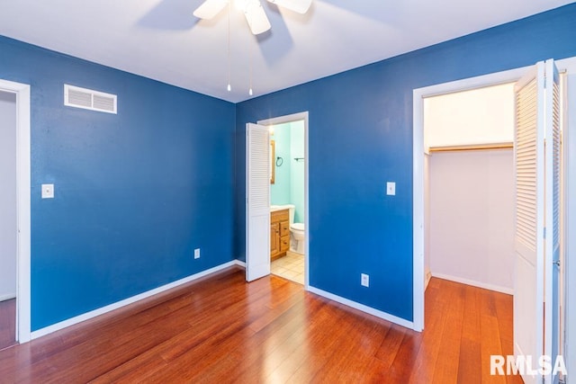 unfurnished bedroom with connected bathroom, ceiling fan, a closet, and wood-type flooring