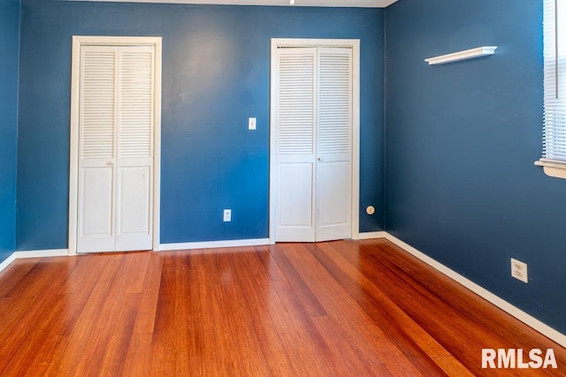 unfurnished bedroom featuring hardwood / wood-style floors and two closets