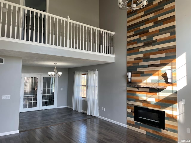 unfurnished living room featuring french doors, a towering ceiling, dark hardwood / wood-style floors, and an inviting chandelier