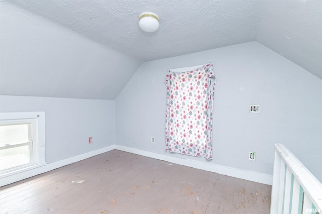 additional living space featuring lofted ceiling, wood-type flooring, a textured ceiling, and baseboards