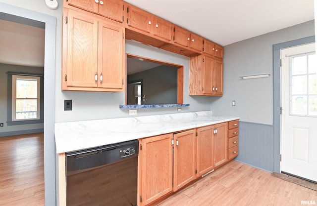 kitchen with black dishwasher, light stone counters, light wood-style flooring, and wainscoting