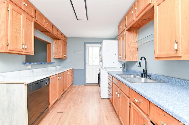 kitchen with a sink, black dishwasher, light countertops, light wood finished floors, and stacked washer and clothes dryer