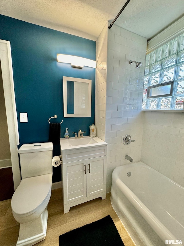 full bathroom with tiled shower / bath combo, a textured ceiling, toilet, vanity, and hardwood / wood-style flooring