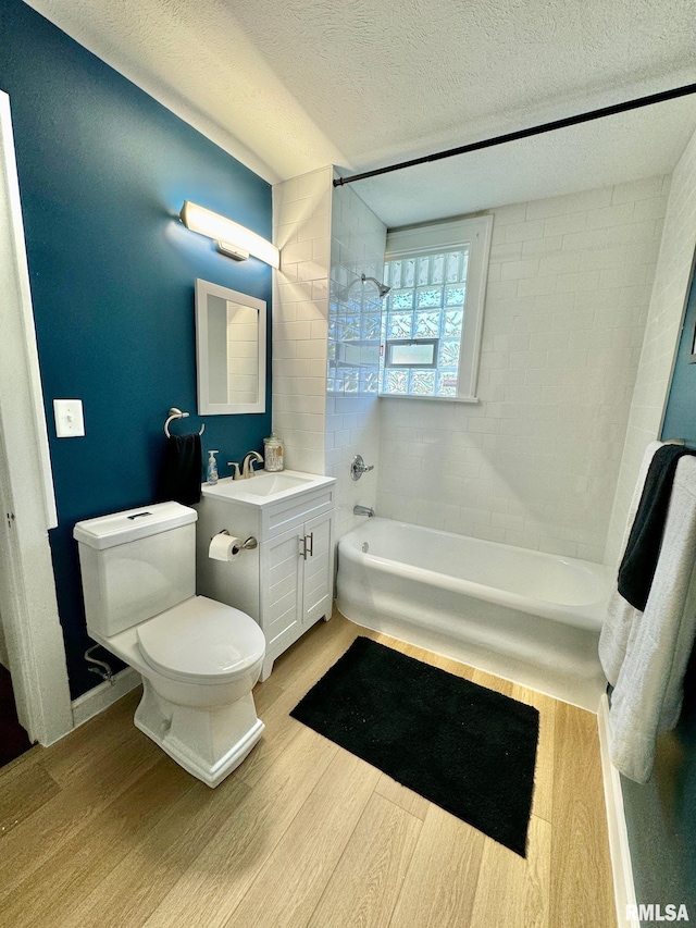 full bathroom with hardwood / wood-style floors, vanity, tiled shower / bath, toilet, and a textured ceiling