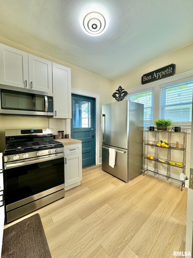 kitchen featuring backsplash, a textured ceiling, stainless steel appliances, light hardwood / wood-style flooring, and white cabinets