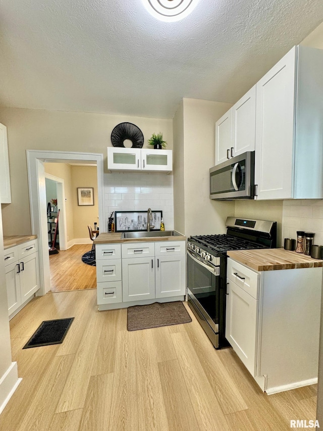 kitchen featuring wooden counters, appliances with stainless steel finishes, tasteful backsplash, light hardwood / wood-style floors, and white cabinetry