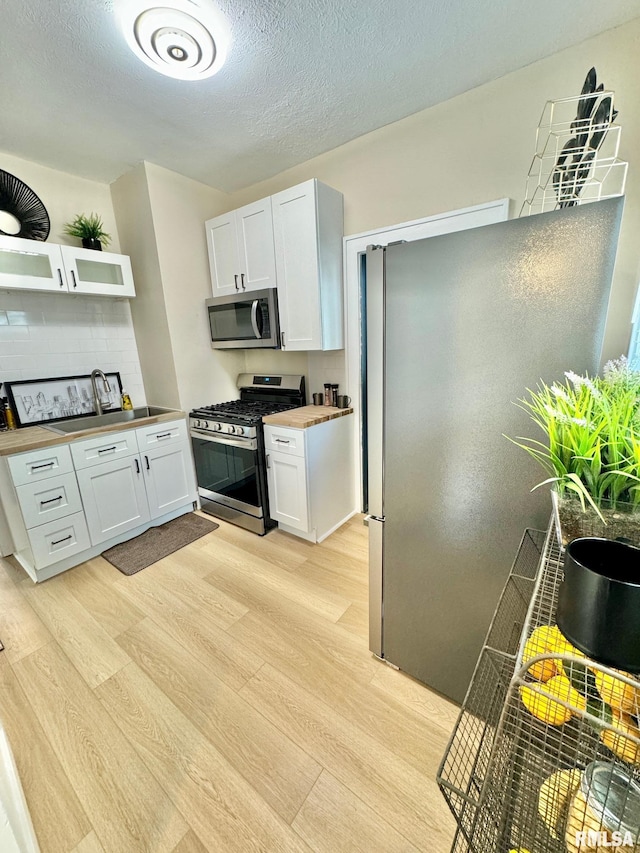 kitchen featuring stainless steel appliances, butcher block countertops, light hardwood / wood-style floors, a textured ceiling, and white cabinets