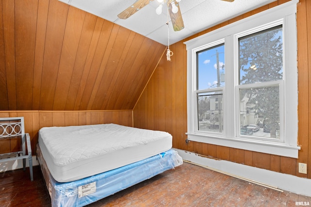 bedroom featuring hardwood / wood-style flooring, ceiling fan, wooden walls, and vaulted ceiling