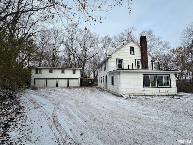 snow covered rear of property featuring a garage and an outdoor structure