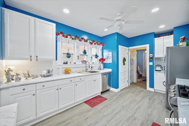 kitchen with appliances with stainless steel finishes, light wood-type flooring, backsplash, sink, and white cabinetry