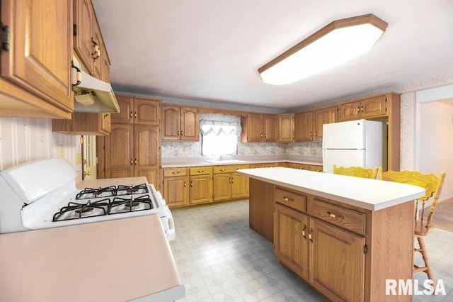 kitchen featuring a breakfast bar, a center island, white appliances, and sink