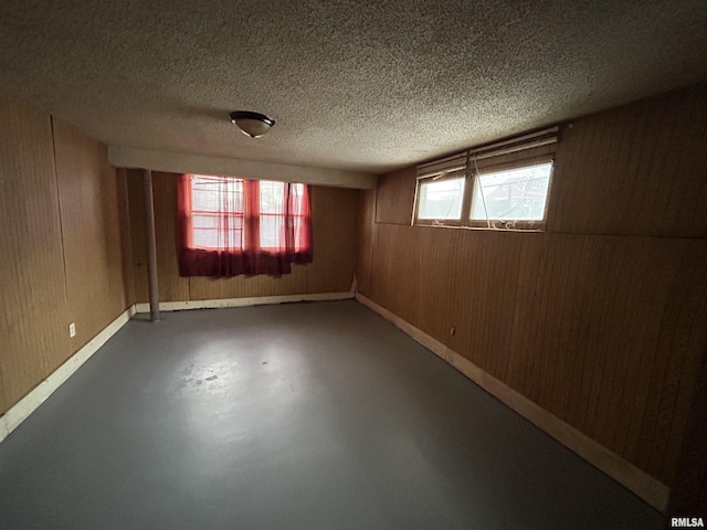 spare room with a wealth of natural light, wood walls, concrete flooring, and a textured ceiling