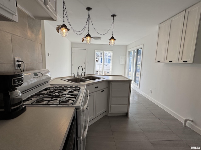 kitchen featuring gas stove, sink, pendant lighting, dark tile patterned flooring, and white cabinetry