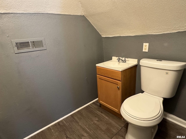 bathroom featuring hardwood / wood-style floors, vanity, vaulted ceiling, toilet, and a textured ceiling