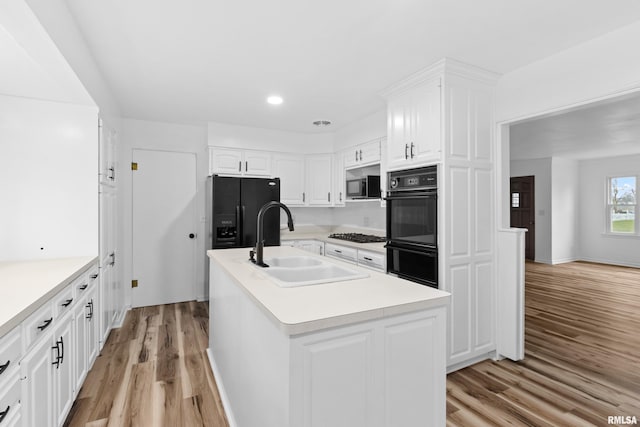 kitchen with a kitchen island with sink, black appliances, white cabinets, sink, and light hardwood / wood-style flooring