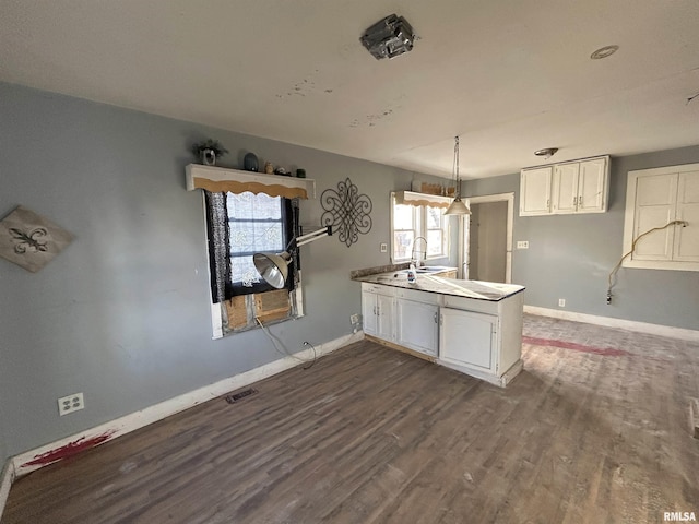 kitchen featuring kitchen peninsula, sink, wood-type flooring, pendant lighting, and white cabinetry