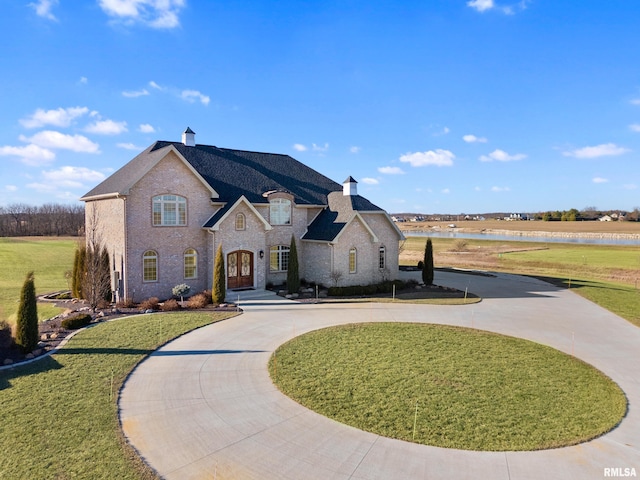 french provincial home with a chimney, curved driveway, and a front lawn