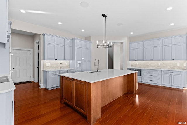 kitchen featuring a sink, a center island with sink, light countertops, and dark wood-style flooring