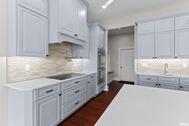 kitchen featuring dark wood-style flooring, black electric stovetop, backsplash, double oven, and a sink