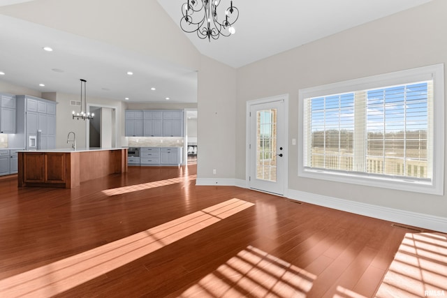 unfurnished living room with a chandelier, visible vents, dark wood finished floors, and baseboards