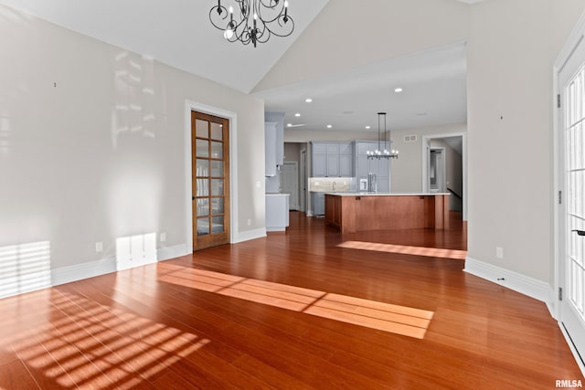 unfurnished living room featuring high vaulted ceiling, recessed lighting, dark wood-type flooring, baseboards, and an inviting chandelier