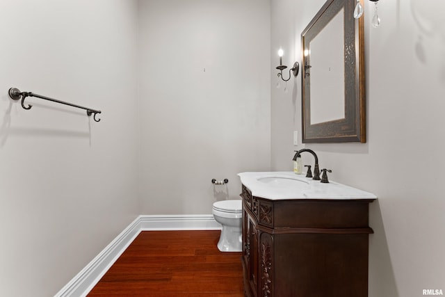 half bath with toilet, wood finished floors, vanity, and baseboards