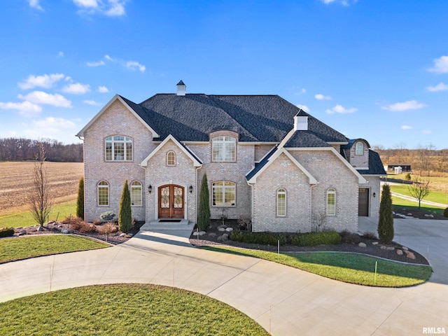 french provincial home with a front lawn, concrete driveway, a chimney, and french doors