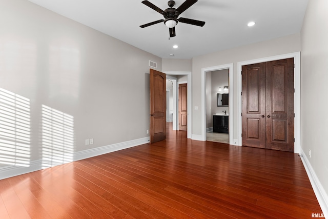 unfurnished bedroom featuring ensuite bath, wood finished floors, visible vents, and baseboards