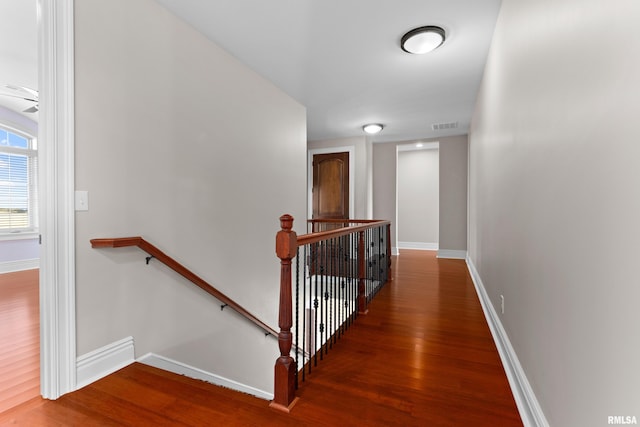 corridor featuring baseboards, visible vents, wood finished floors, and an upstairs landing