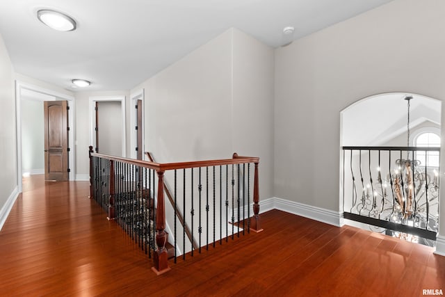 hall featuring wood-type flooring, baseboards, a notable chandelier, and an upstairs landing