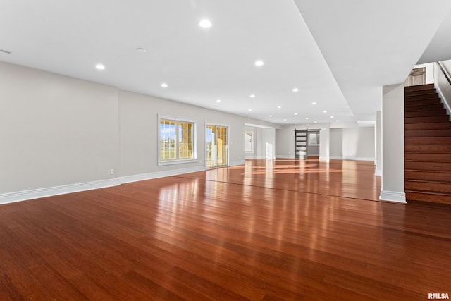 unfurnished living room featuring baseboards, stairway, wood finished floors, and recessed lighting