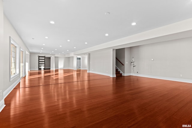 unfurnished living room with a barn door, recessed lighting, wood finished floors, baseboards, and stairs