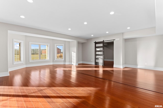 unfurnished living room with baseboards, a barn door, wood-type flooring, and recessed lighting