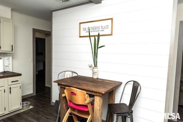 dining room with wooden walls, dark wood-type flooring, and ornamental molding