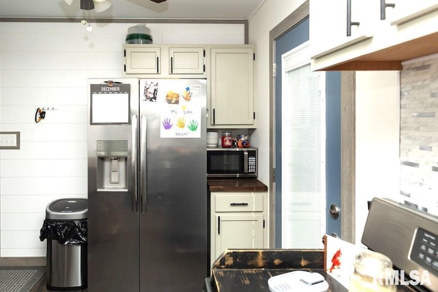 kitchen featuring cream cabinetry, appliances with stainless steel finishes, ceiling fan, and wooden walls