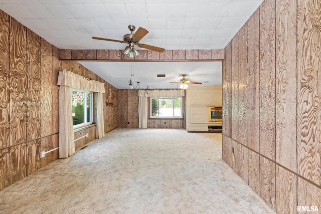 unfurnished living room with wooden walls, light colored carpet, ceiling fan, and a healthy amount of sunlight