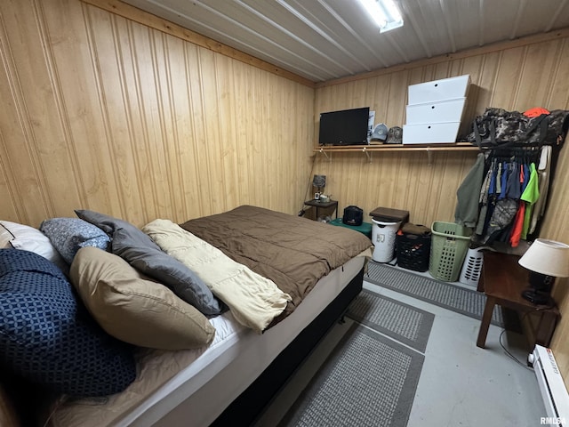 bedroom with wood walls, concrete flooring, and a baseboard heating unit