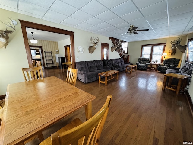 dining space featuring a drop ceiling, ceiling fan, and dark wood-type flooring