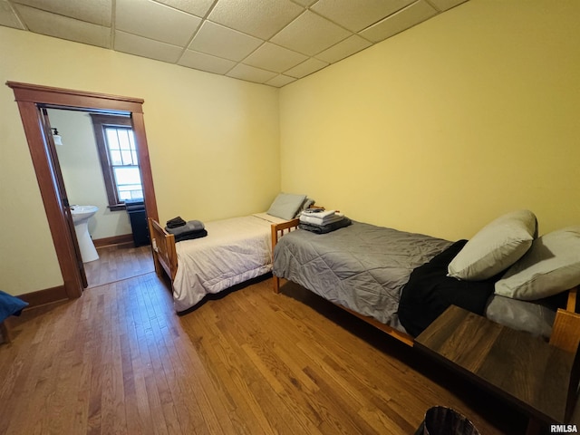 bedroom featuring a paneled ceiling, hardwood / wood-style flooring, and connected bathroom