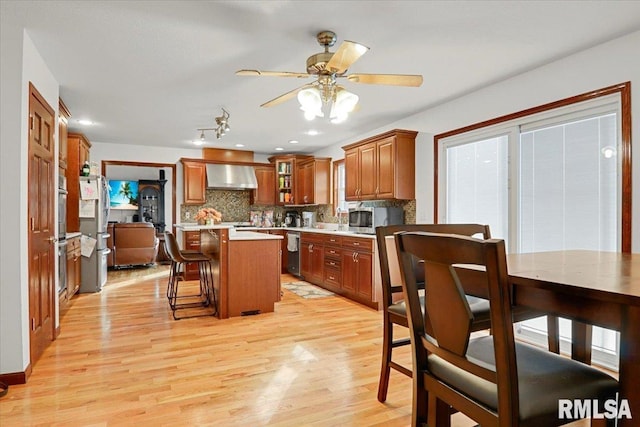 kitchen featuring a kitchen bar, wall chimney exhaust hood, stainless steel appliances, light hardwood / wood-style floors, and a kitchen island