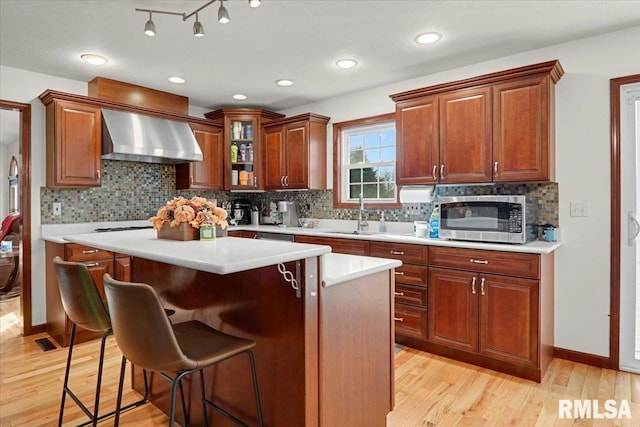 kitchen with decorative backsplash, wall chimney exhaust hood, sink, light hardwood / wood-style flooring, and a center island