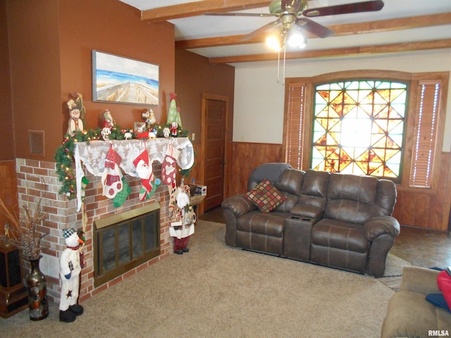 living room with beam ceiling, ceiling fan, a brick fireplace, carpet floors, and wooden walls