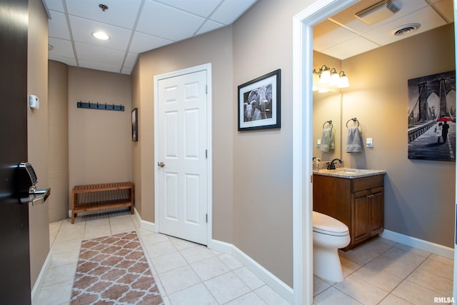 bathroom with tile patterned flooring, vanity, toilet, and a drop ceiling