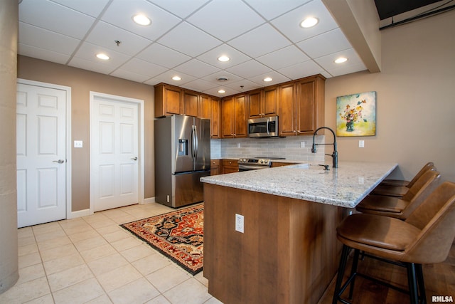 kitchen with kitchen peninsula, a kitchen breakfast bar, light stone counters, stainless steel appliances, and sink