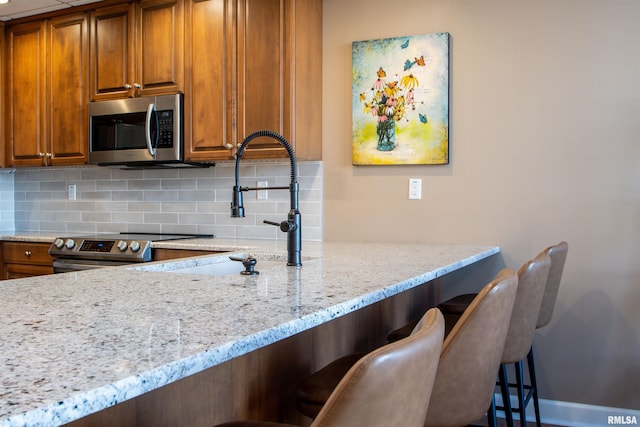 kitchen with sink, decorative backsplash, light stone counters, a breakfast bar area, and stainless steel appliances