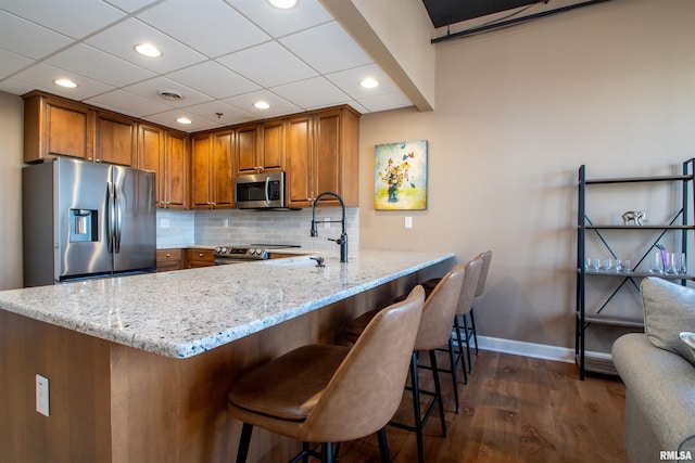 kitchen featuring a kitchen breakfast bar, kitchen peninsula, light stone countertops, and appliances with stainless steel finishes